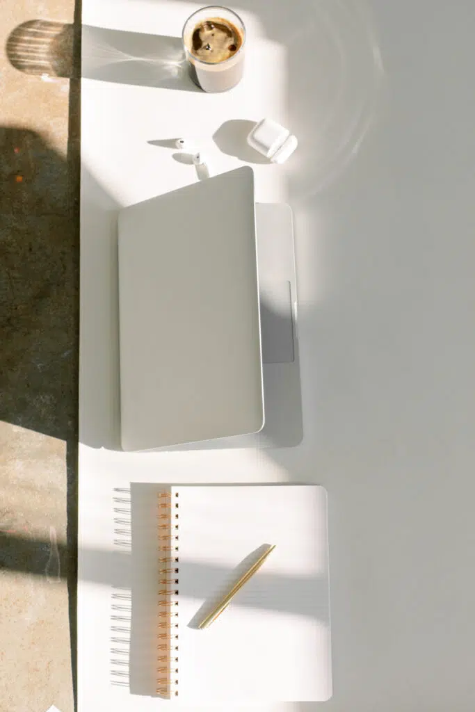 Image of iced coffee, airpods, laptop, amd notebook with pen.
