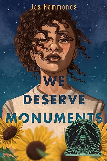Image of book cover. Jas Hammonds. We Deserve Monuments. Seal for Coretta Scott King John Steptoe Award New Talent Winner. Drawing of African American teenage girl with night sky in the background and sunflowers in the foreground.
