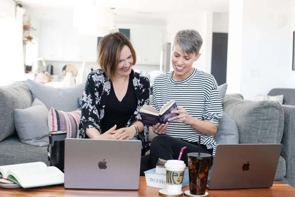 Kate and Stephanie sitting on couch, open books and laptops on the table in front of them.