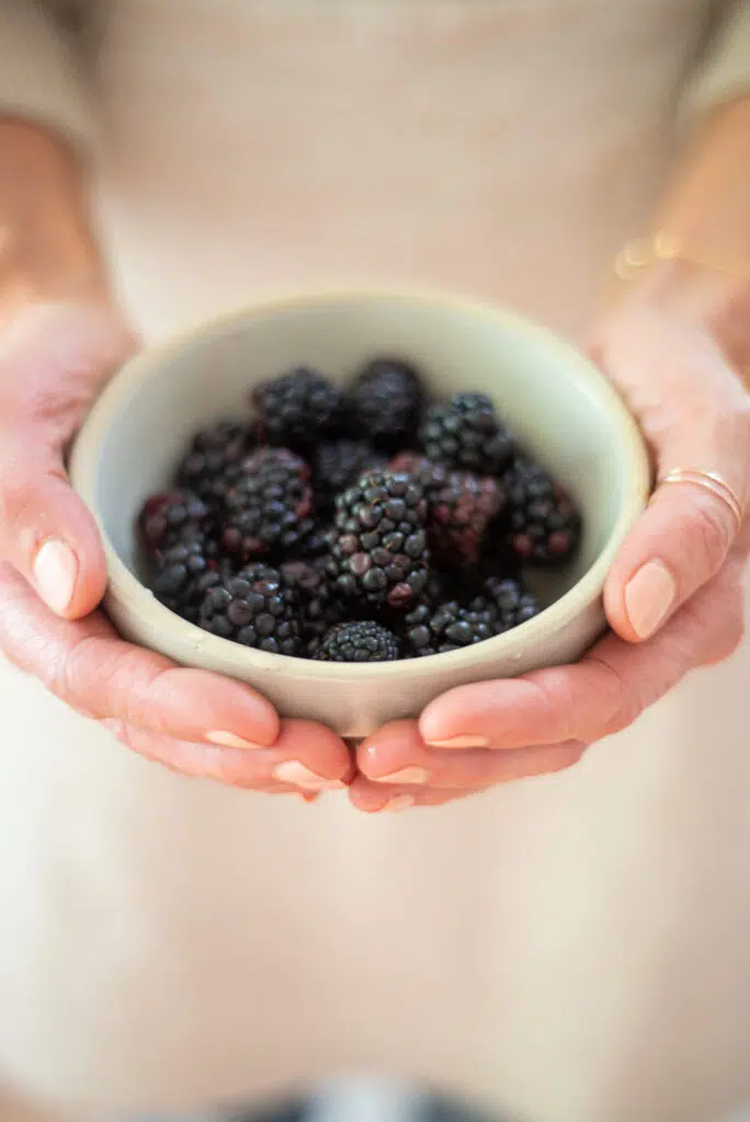 Blackberries in a small ceramic bowl cradled in a person's hands.
