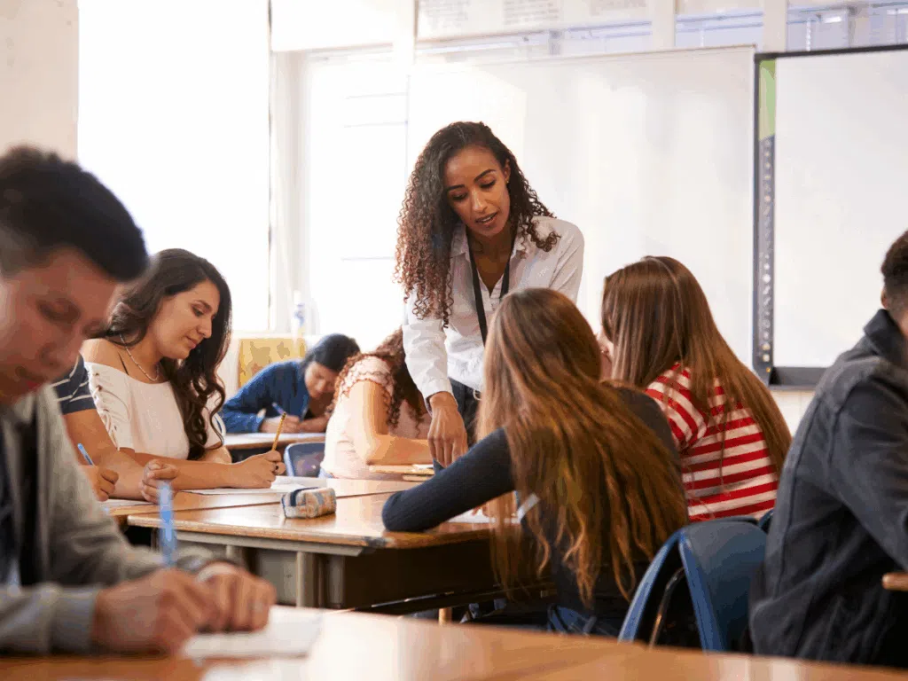 Teacher speaking to two students in high school English classroom.