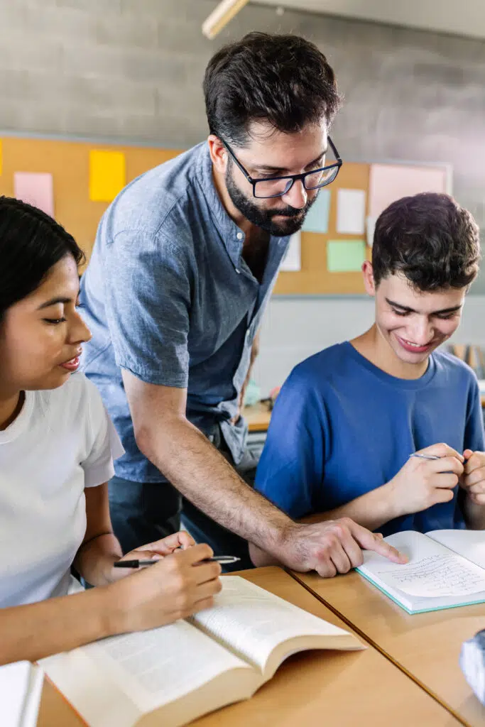 A teacher works closely with two students as they annotate a poem, using guided questions and discussion to support poetry analysis while teaching tone in literature.