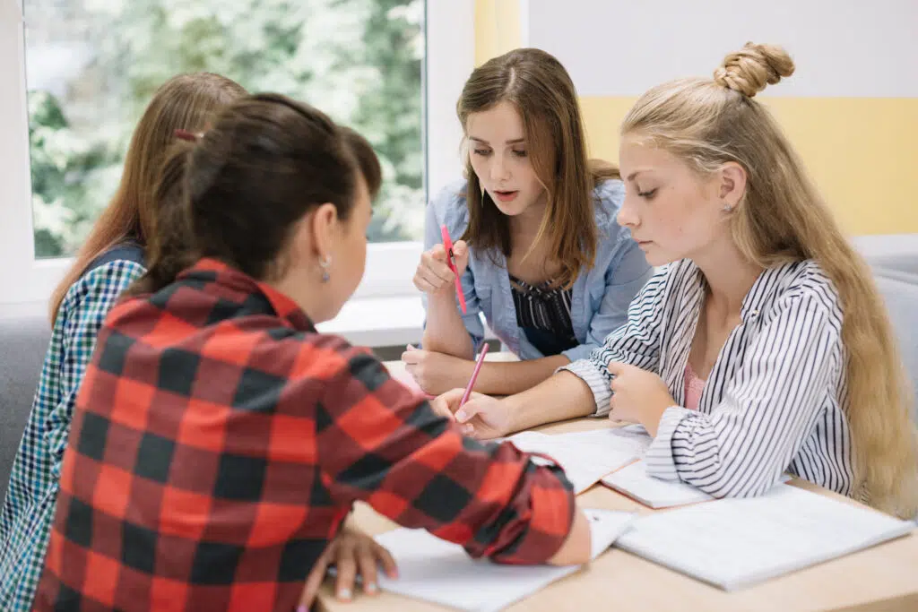Students collaborate at a desk during a writing lesson, discussing ideas and practicing embedding quotes into their written responses.